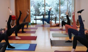 Pilates class with participants performing leg lifts on mats in a well-lit studio. Focus on core str.