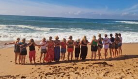 People practicing yoga on the sandy beach with ocean waves in the background.