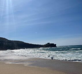 Scenic coastal view with sandy beach, waves, and cliffs, perfect for outdoor Pilates or wellness act.