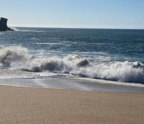 Beach waves crashing on sandy shore with cliffs in the background.